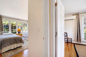Une chambre à coucher avec un lit, une table de chevet, une lampe et une chaise. Il y a une fenêtre avec des rideaux et un appareil de climatisation fixé au mur.