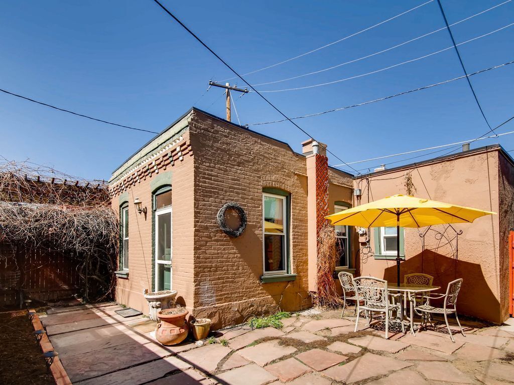 A brick building with a patio area featuring a table and chairs under a yellow umbrella.