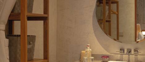A bathroom with a wooden shelf, a round mirror, and a sink with toiletries.