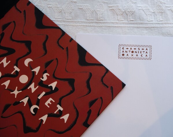 A red book with white text titled 'ANTONIETA' and a white envelope with a stamp. - Casa Antonieta (Oaxaca)