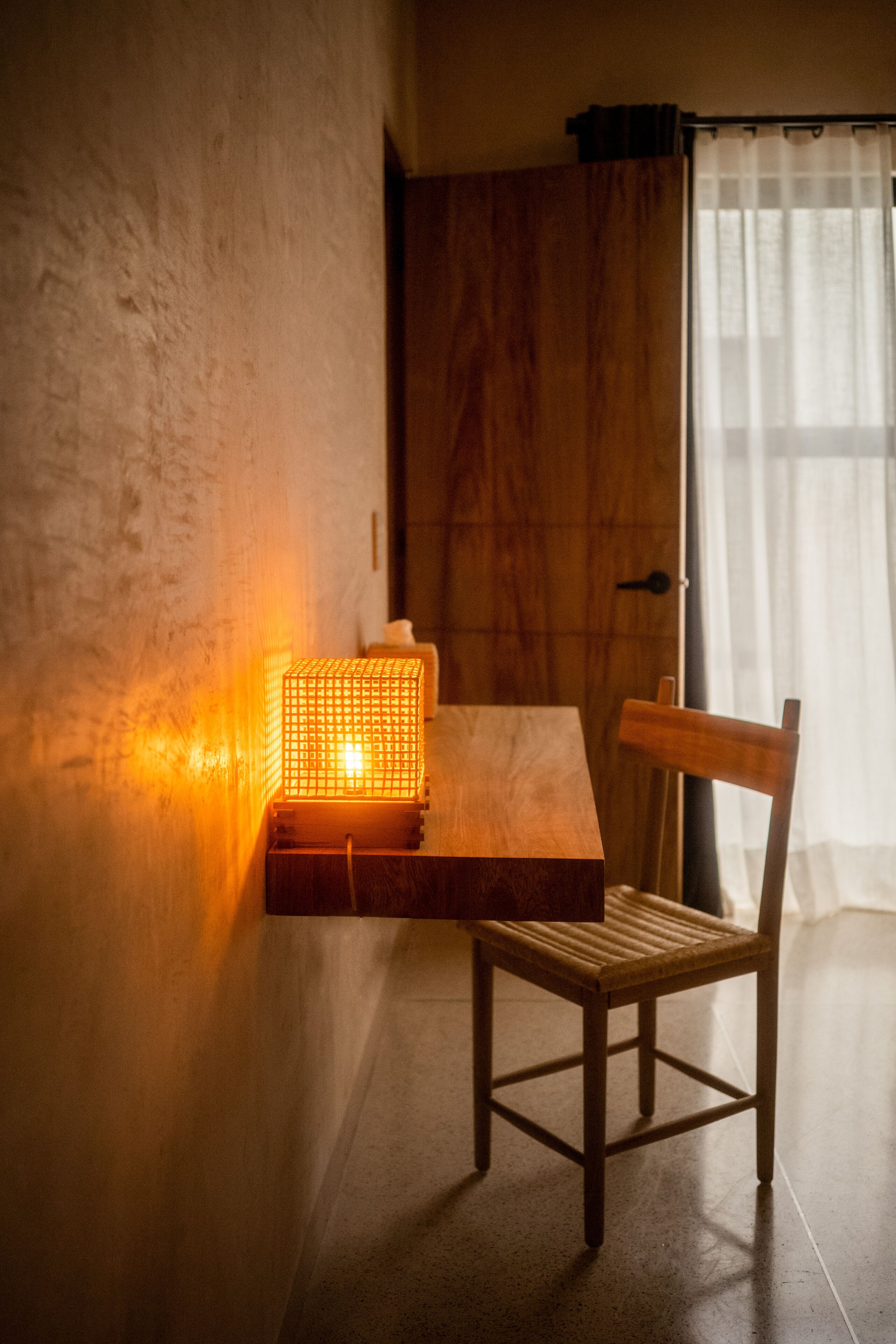 Een houten stoel en een tafel met een lamp in een kamer met een structuurwand en een houten deur.