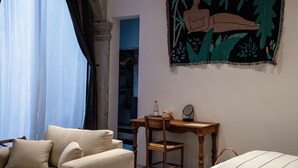 A room with a bed, a desk, a chair, a window with curtains, and a tapestry on the wall. - Casa Antonieta (Oaxaca)