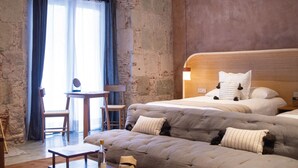 A hotel room with a large bed, a sofa, a small table, and a chair. There is a window with curtains and a view of the outside. - Casa Antonieta (Oaxaca)