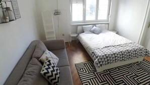Makuuhuoneessa on sänky, sohva, pieni jakkara, seinälle ripustettu teline ja kuviollinen matto.