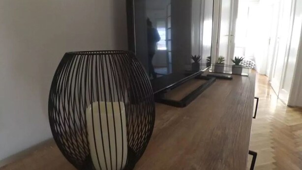 Moderni olohuone, jossa on suuri litteänäyttöinen televisio, musta metallirunkoinen tuoli ja puulattia.