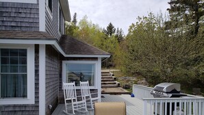 Une terrasse avec un barbecue, des chaises blanches et une table.