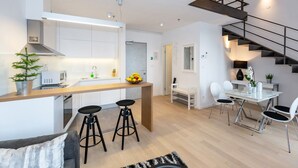 Una cocina moderna con una isla central, una zona de comedor con mesa y sillas, y una escalera con barandilla de metal.