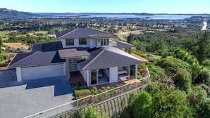 A modern two-story house with a large garage, a covered patio, and a scenic view of a lake and forested area. - Tihi Retreat - Rotorua (Rotorua Township)