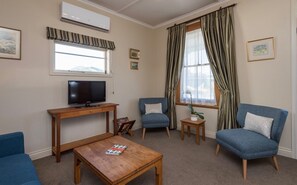 A living room with a television, two blue armchairs, a wooden coffee table, and a window with curtains. - Spoil yourself at Strupak Cottage, a quiet retreat close to the city (Nelson City)