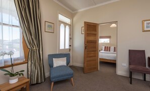 A room with a bed, a chair, a window with curtains, and a door leading to another room. - Spoil yourself at Strupak Cottage, a quiet retreat close to the city (Nelson City)