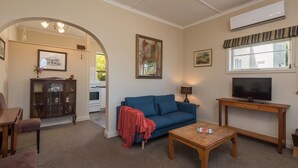 A living room with a blue sofa, a wooden coffee table, a TV on a wooden stand, and a cabinet. - Spoil yourself at Strupak Cottage (Nelson City)