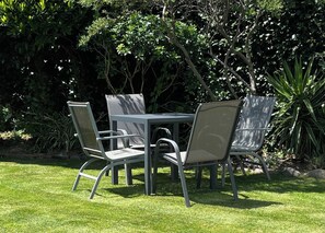 A patio with a table and four chairs, surrounded by greenery. - Spoil yourself at Strupak Cottage, a quiet retreat close to the city (Nelson City)