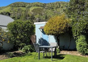 A garden with a table and chairs, surrounded by greenery and a hillside in the background. - Spoil yourself at Strupak Cottage, a quiet retreat close to the city (Nelson City)