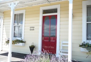 A yellow building with a red door, white window frames, and a porch with white railings. - Spoil yourself at Strupak Cottage, a quiet retreat close to the city (Nelson City)