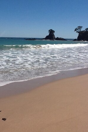 Una playa con agua azul cristalina, olas y formaciones rocosas.