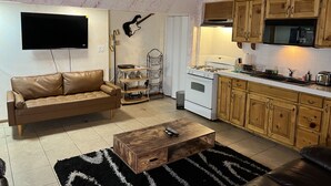 A living room with a brown leather sofa, a wooden coffee table, a TV, and a kitchen with wooden cabinets and a stove. - SPACIOUS  ONE  BEDROOM APARTMENT VERY CLOSE TO VENICE BEACH with washer /dryer (Los Angeles)