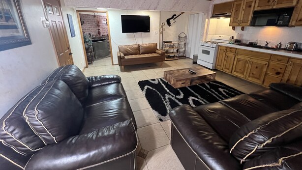 A living room with a brown leather sofa, a wooden coffee table, and a kitchen area with wooden cabinets and a stove. - SPACIOUS  ONE  BEDROOM APARTMENT VERY CLOSE TO VENICE BEACH with washer /dryer (Los Angeles)