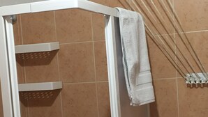 Área de duche com azulejos castanhos, cabine de duche branca e uma toalha pendurada na porta.