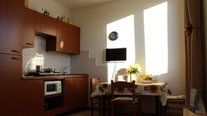 Uma cozinha com armários de madeira, micro-ondas, mesa de jantar com cadeiras e um relógio na parede.