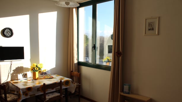 Uma sala de jantar com uma mesa posta para quatro pessoas, um relógio na parede e uma janela com cortinas.