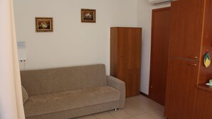 Um quarto com um sofá bege, um guarda-roupa de madeira e duas imagens emolduradas na parede.