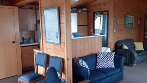 A cozy cabin interior with a living area featuring a blue sofa, striped armchair, and a small dining table with a blue bowl.