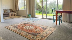 Una habitación amplia con un gran ventanal corredera que da a un balcón, una mesa de comedor con sillas y una alfombra estampada en el suelo.