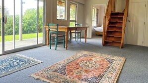Una habitación con una mesa de comedor, sillas, una escalera y grandes puertas de vidrio que dan a un jardín.