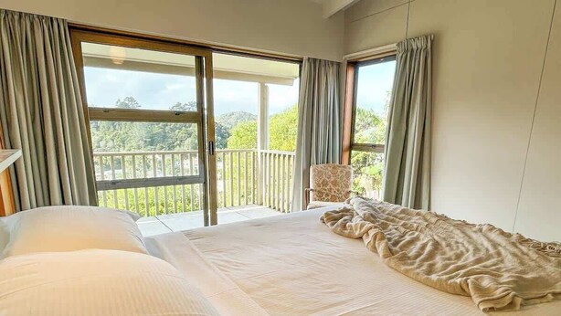 Habitación de hotel con una cama grande, una silla y un balcón con vistas a zonas verdes.