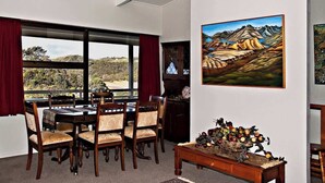 Un comedor con una mesa y sillas, una araña, un cuadro y una composición decorativa de frutas.