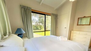 Una habitación de hotel con una cama grande, un aparador, una lámpara y una ventana con cortinas.