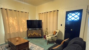 A living room with a sofa, a TV, a ceiling fan, a door, and a window. - Grand Canyon & Route 66: Historic Williams Getaway (Williams)
