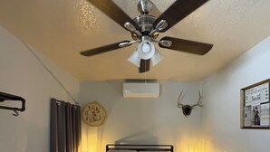 A bedroom with a bed, a ceiling fan, an air conditioning unit, a wall-mounted clock, and a framed picture. - Grand Canyon & Route 66: Historic Williams Getaway (Williams)