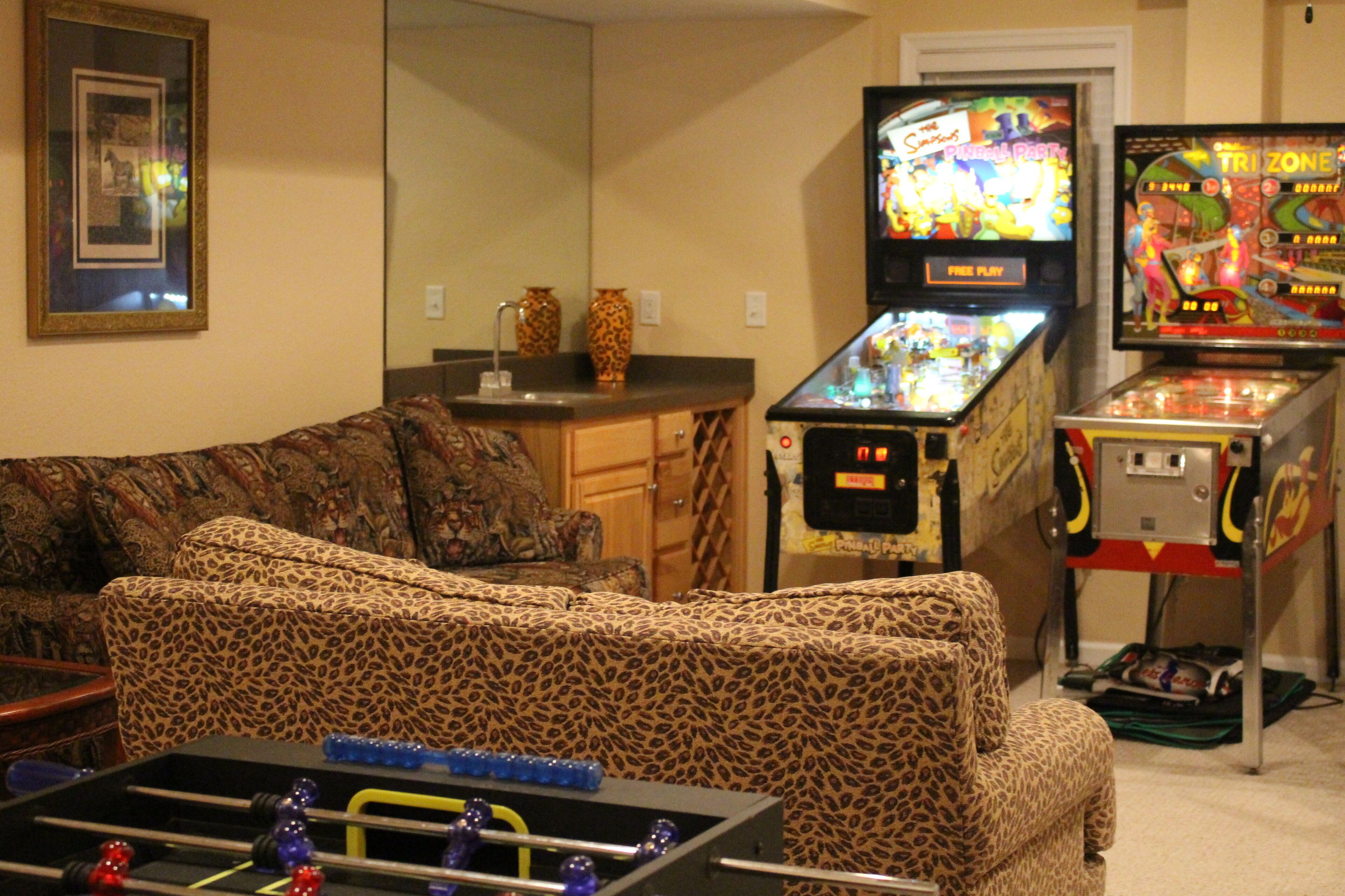 A living room with a sofa, two arcade games, and a foosball table.