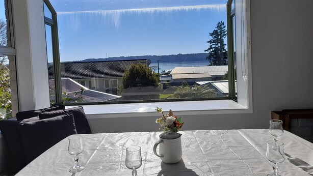 Une table à manger donnant sur un paysage côtier grâce à une grande fenêtre.