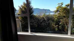 Une chambre avec un lit, une fenêtre donnant sur un paysage montagneux et des arbres.