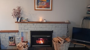 Une cheminée avec un manteau en briques blanches, un tableau encadré au-dessus, et un téléviseur sur le côté droit.