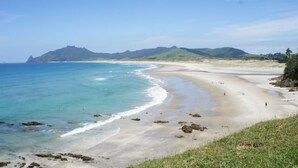 A beach with clear blue water, sandy shore, and distant hills. - Cliffhouse, Taiharuru, Northland (Whangarei Heads)