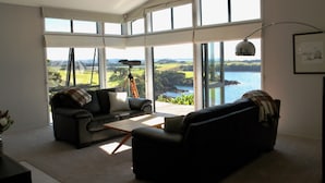 A spacious living room with large windows offering a view of the sea and hills. - Cliffhouse, Taiharuru, Northland (Whangarei Heads)