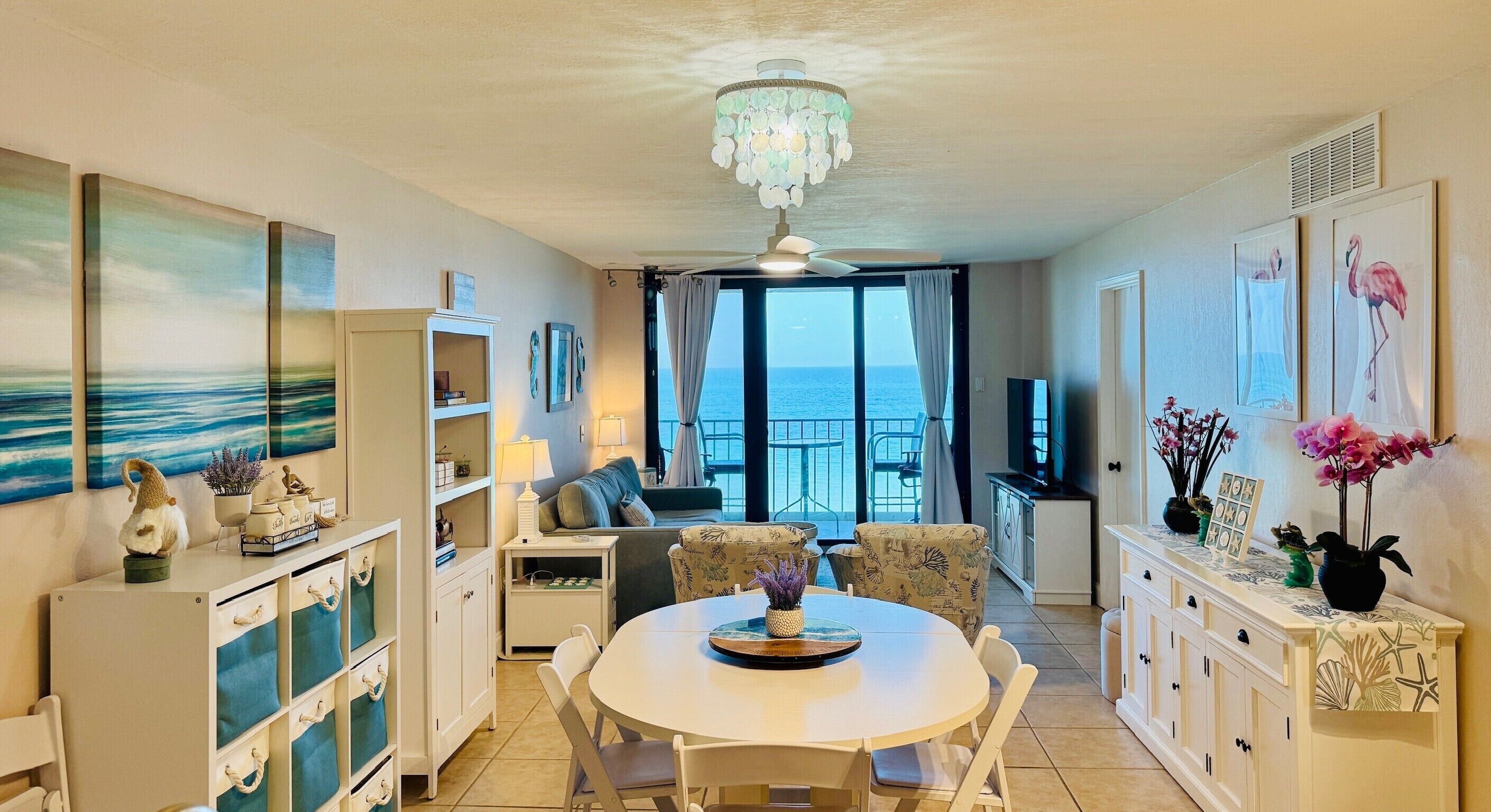 Una habitación bien iluminada con una mesa de comedor, sillas, un sofá y vista al mar a través de un ventanal grande.