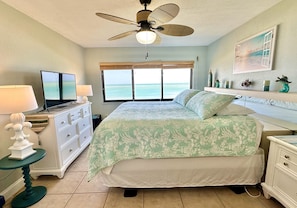 A bedroom with a bed, a television, a dresser, a nightstand, a ceiling fan, and a window with a view of the ocean. - Beautiful Ocean-front Condo with Stunning Views (Fort Pierce)