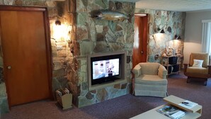 Ein Steinkamin mit Fernseher, ein Holzstuhl und ein kleiner Tisch mit Zeitschriften.