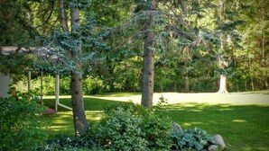 Ein gepflegter Garten mit verschiedenen Bäumen und Sträuchern, einem deutlichen Weg und einer kleinen Struktur im Hintergrund.