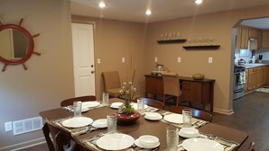Ein Esszimmer mit gedecktem Tisch für sechs Personen, im Hintergrund eine Küche und eine Tür zu einem weiteren Raum.