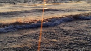 En strand i solnedgang med bølger og et fjerntliggende landskab.