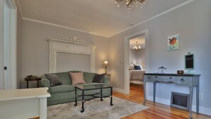 Un salon avec un canapé vert, une table basse, une petite table d’appoint blanche et une console surmontée d’une lampe.