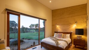 Un dormitorio con un amplio ventanal corredera que da a un jardín, una cama de madera y una mesita de noche con lámpara.