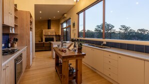 Una cocina moderna con armarios de madera, una isla central y grandes ventanales con vistas a árboles.