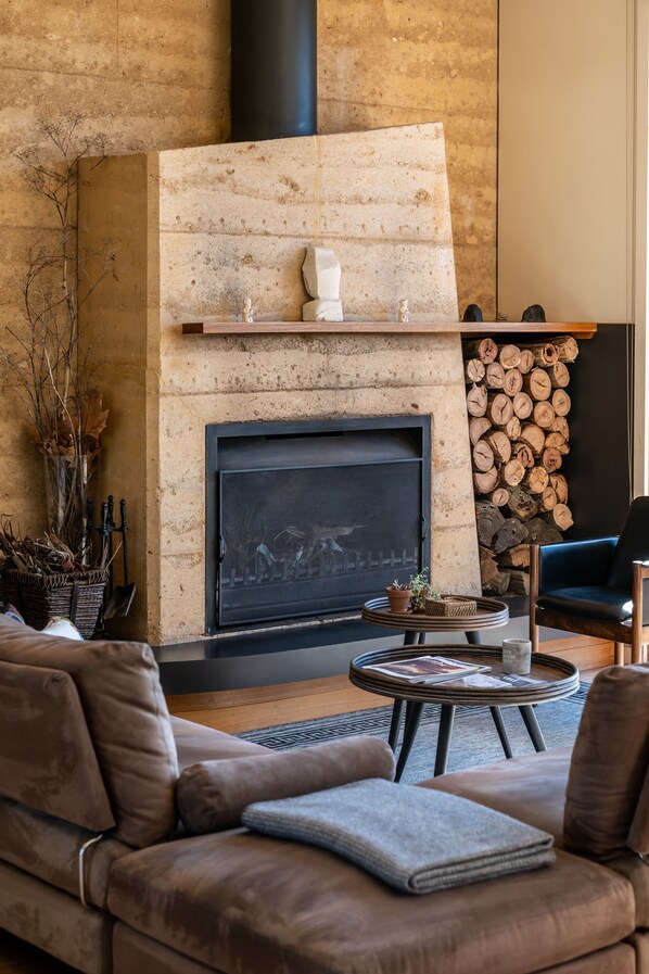 Un salon moderne avec une cheminée, des canapés en cuir, une table basse et une pile de bois de chauffage.