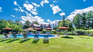 A pool area with lounge chairs and umbrellas, surrounded by a fence and trees. - Perfect Reunion House for 18! 8 bedrooms, 5 baths, Pool, Tennis, Big lawn, Dogs! (Manchester)